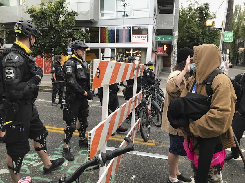caption: Protesters stand across from Seattle officers early Wednesday in a road in the Capitol Hill Organized Protest zone. Police started taking down demonstrators' tents in the protest zone after Seattle's mayor ordered it to be cleared.