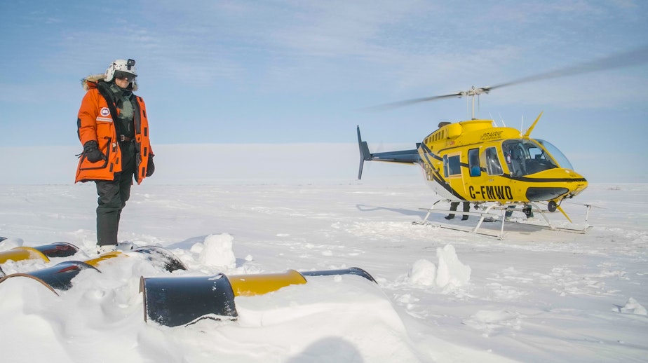 caption: Polar bear researcher David McGeachy standing on the coast of Hudson Bay at a fuel cache to fill up the helicopter with more fuel before heading out to find polar bears.