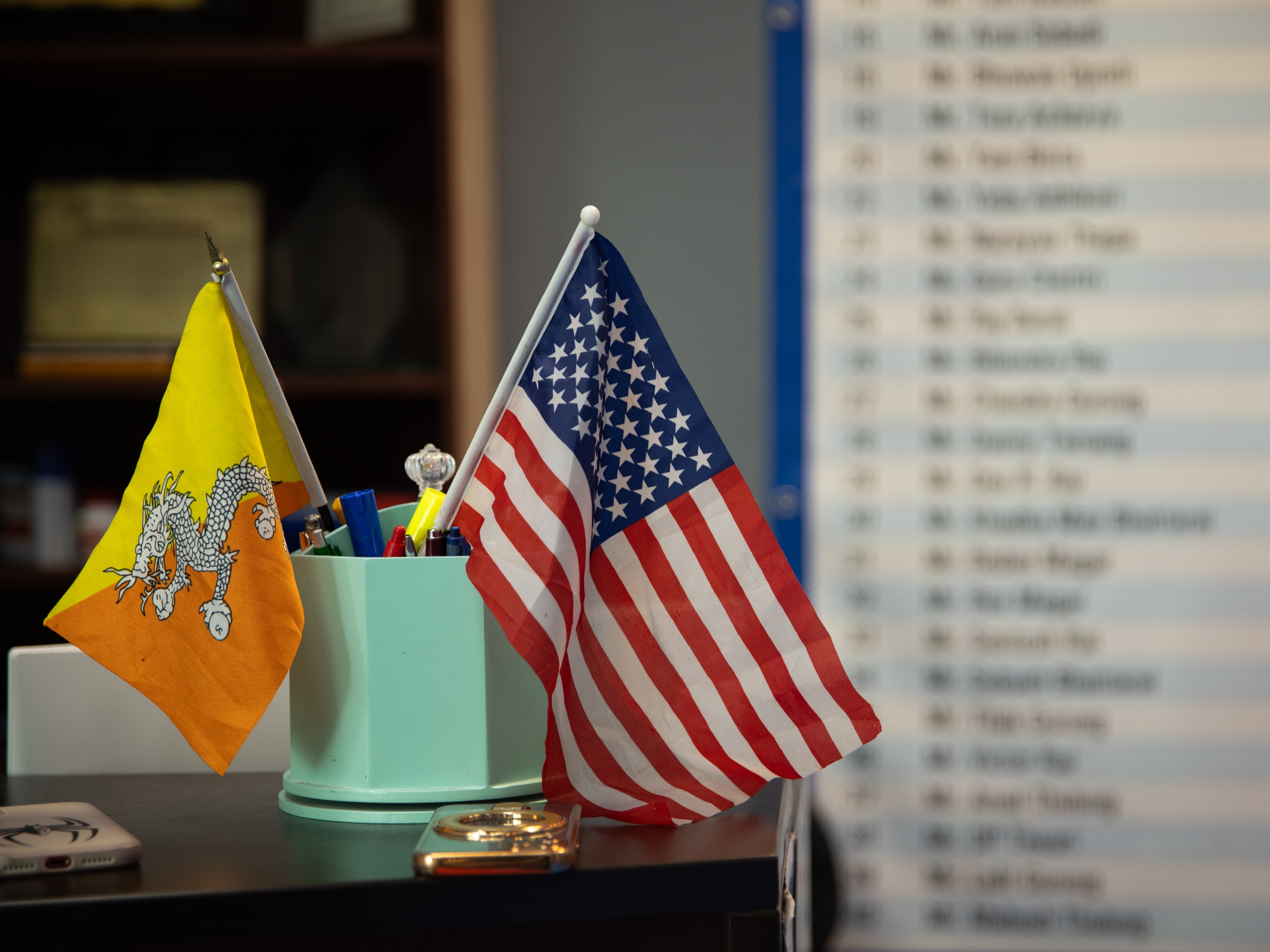 caption: A Bhutanese and American flag are displayed on the desk of a business in Harrisburg, PA on April 16. This is not the first time that Nepali-speaking Bhutanese refugees have faced questions about citizenship and belonging. Some 30 years ago, they were branded as illegal immigrants by the Bhutanese government and were expelled or forced to flee.