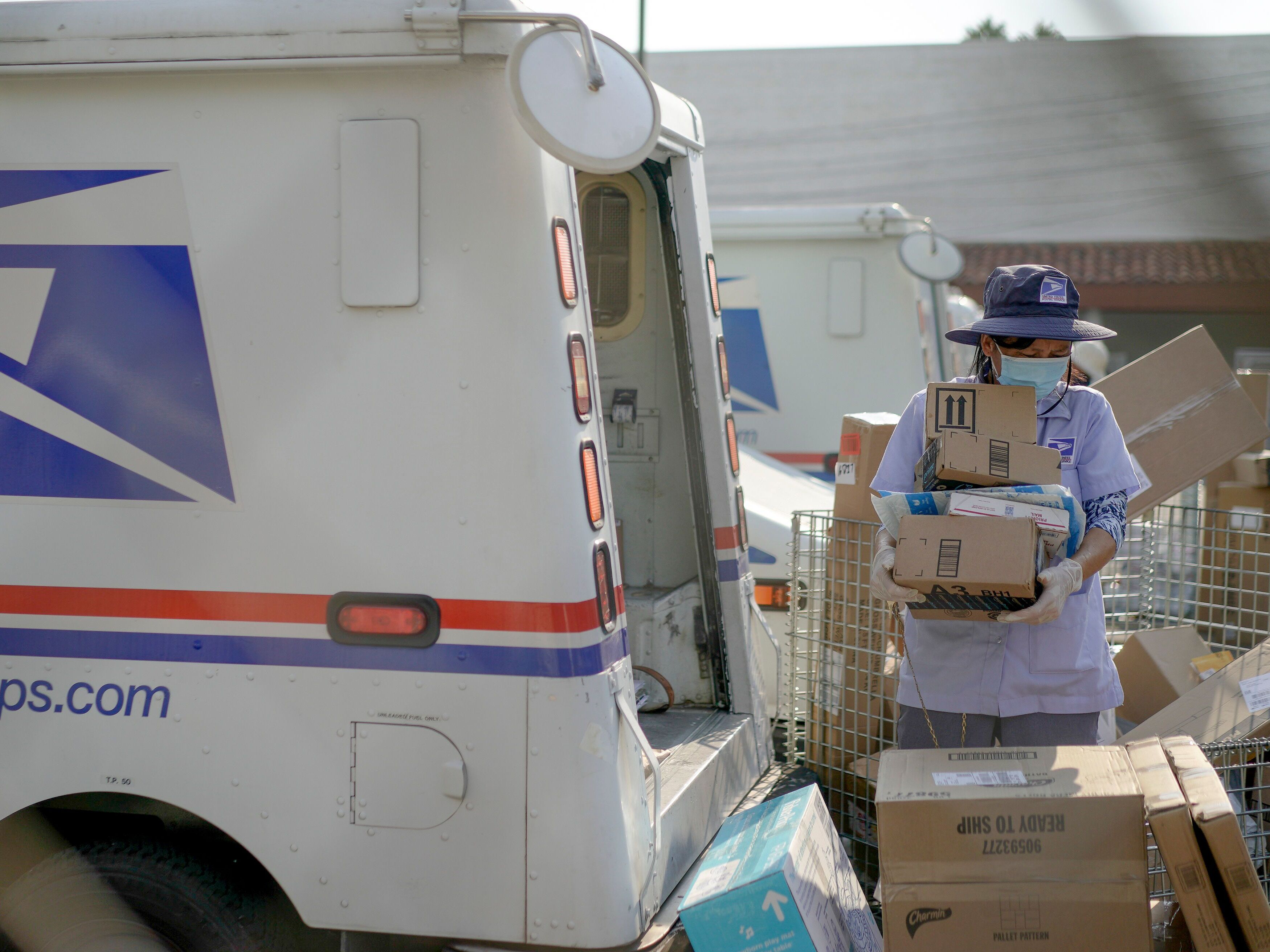 caption: A U.S. Postal Service worker sorts packages behind a mail truck in Los Angeles in 2020.