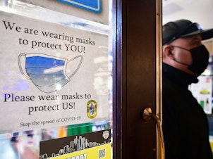 caption: A man wears his mask as he walks past a sign posted on a storefront reminding people to wear masks, on February 25, 2022 in Los Angeles. Los Angeles ends its indoor mask mandate on February 25 for fully vaccinated people with proof of vaccination. Masks are still required for unvaccinated people or those who cannot show proof of a negative test.