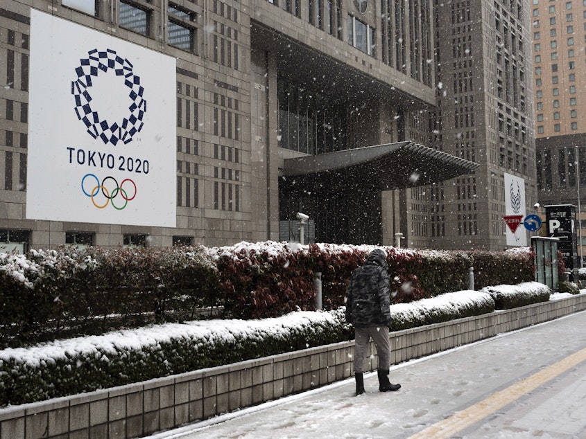 caption: The International Olympic Committee has set firm dates for the delayed Tokyo 2020 Olympics, which will now start in July of 2021. Here, a man walks past a banner promoting the Tokyo 2020 Olympics Sunday, after a late-season snow in Tokyo. Millions of Tokyo residents were asked to stay home this weekend, due to the new coronavirus.