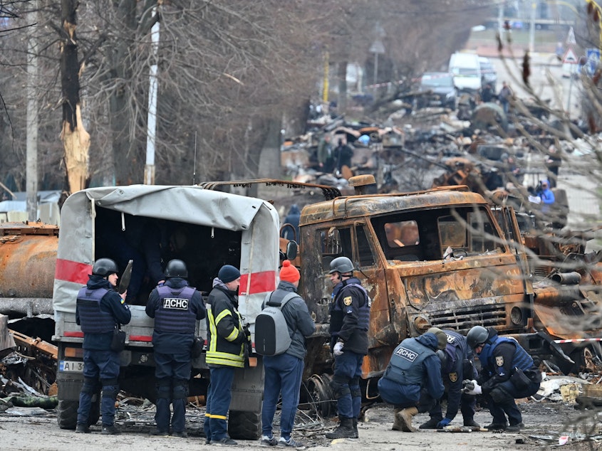caption: Emergency workers conduct mine-clearing operations among destroyed vehicles on a street of Bucha outside of Kyiv last week.