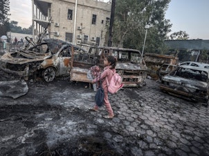 caption: A girl tries to collect usable belongings amid the wreckage of vehicles after the explosion at Al Ahli Arab Hospital in Gaza.