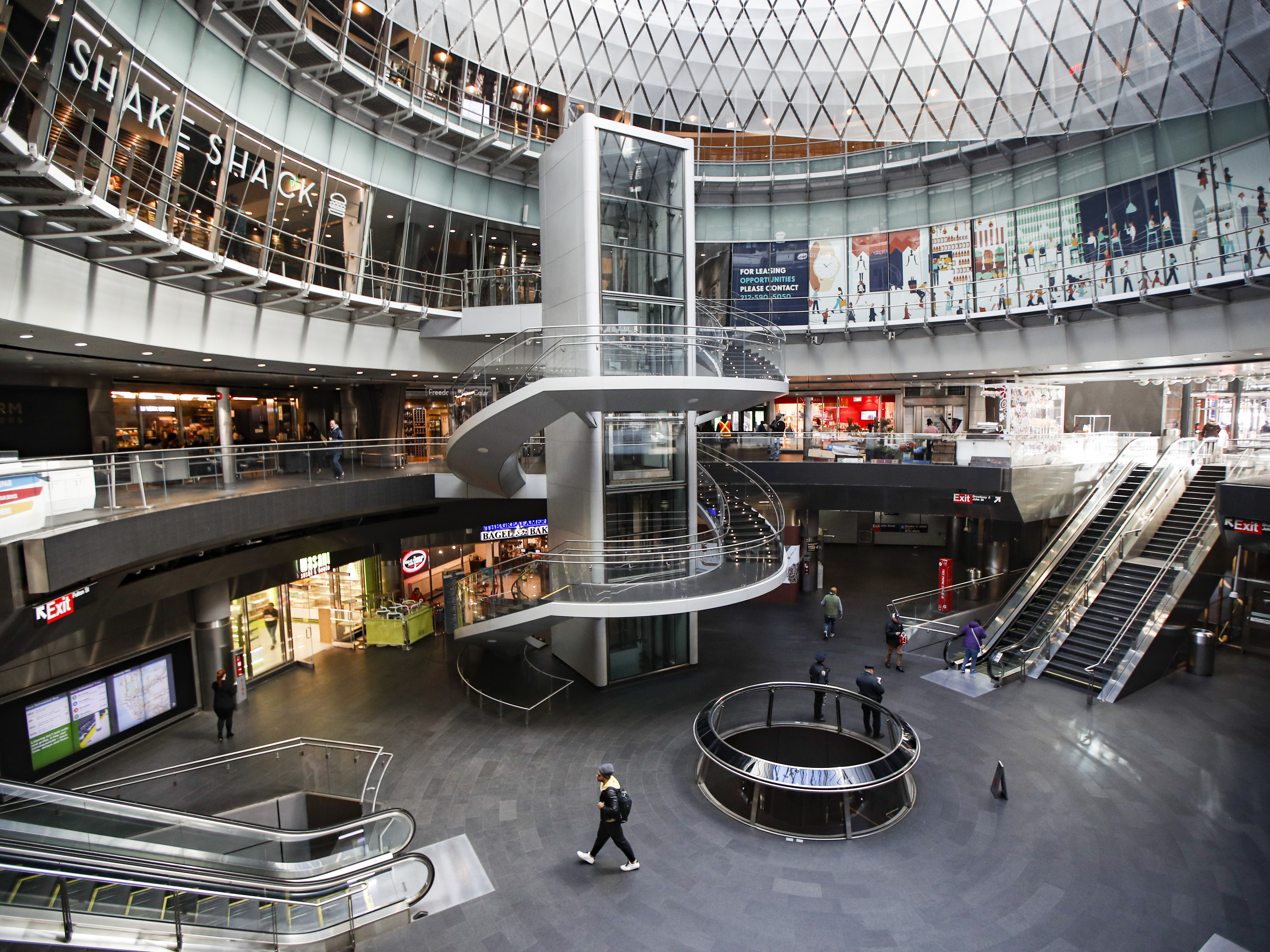 caption: A pedestrian passes a nearly empty subway and retail complex in lower Manhattan as businesses are closed due to coronavirus concerns on Monday.