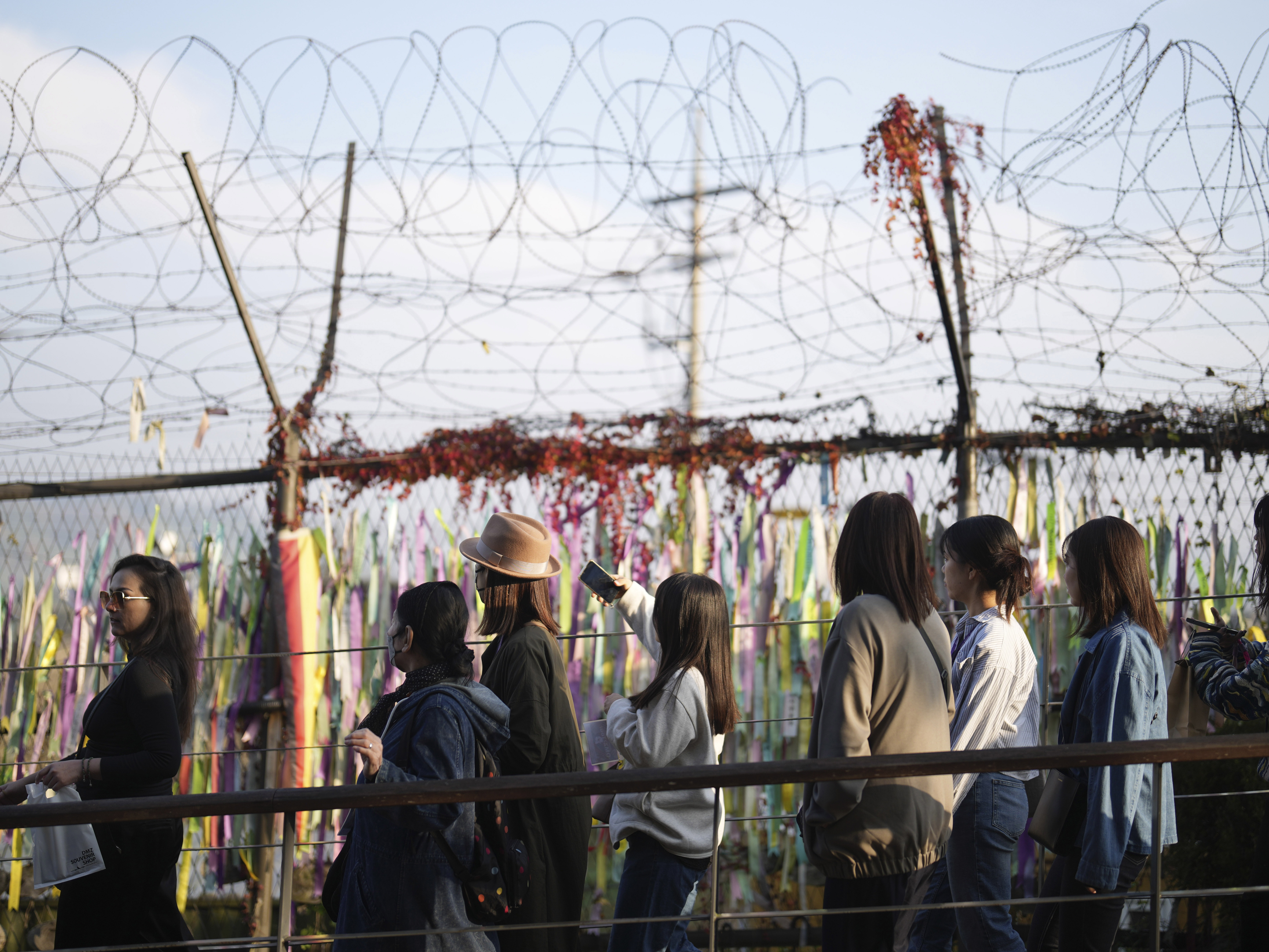 caption: Visitors walk near a wire fence decorated with ribbons written with messages wishing for the reunification of the two Koreas at the Imjingak Pavilion in Paju, South Korea on Thursday.
