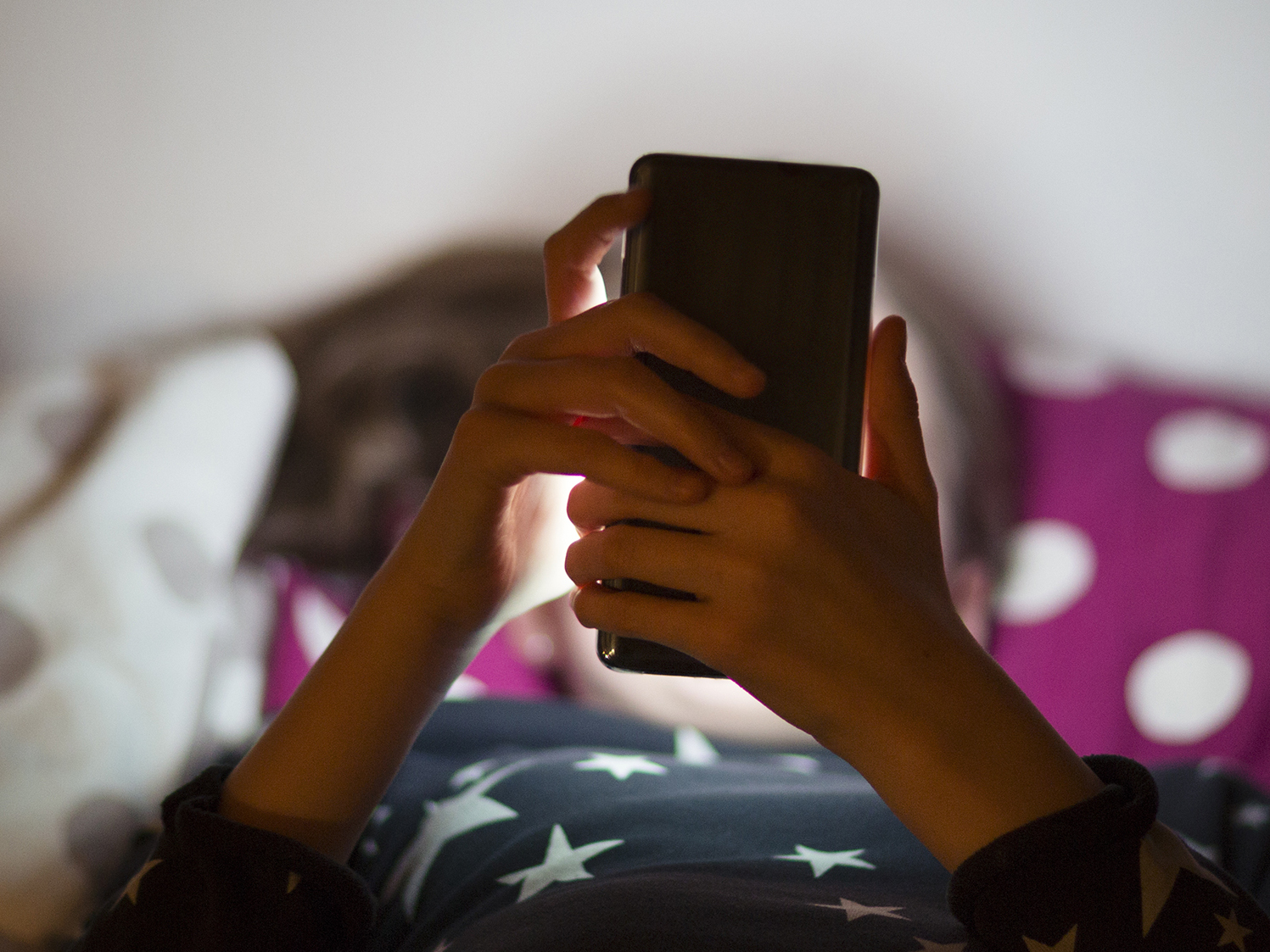 caption: Snapchat is rolling out new parental controls that allow parents to see their teenager's contacts and confidentially report to the social media company any accounts that concern them. A child lies in bed illuminated by the glow of a cell phone.