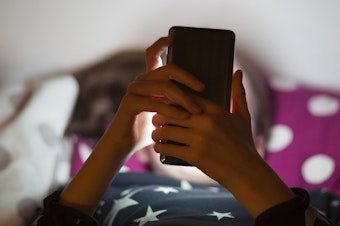 caption: Snapchat is rolling out new parental controls that allow parents to see their teenager's contacts and confidentially report to the social media company any accounts that concern them. A child lies in bed illuminated by the glow of a cell phone.