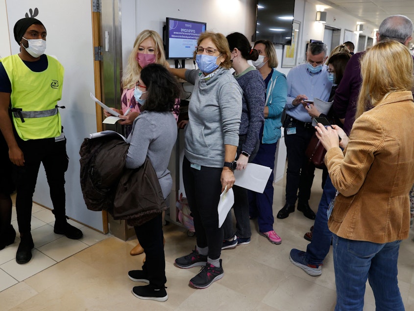 caption: Staff volunteers queue to receive a fourth dose of the Pfizer COVID-19 vaccine at the Sheba Medical Center in Israel on Dec. 27, 2021, as the hospital conducted a trial of a fourth jab of the vaccine.