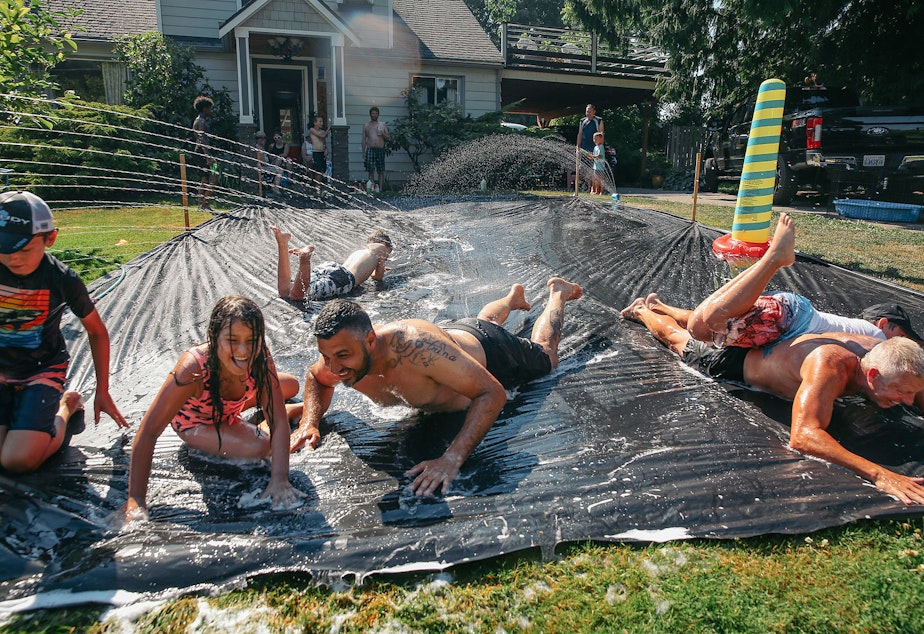 caption: Vasili Vouros, center, and John Cain Jr., right, slip n' slide with their kids in Vouros's front yard on Monday, June 28, 2021, in Skyway. The National Weather Service recorded 108 degrees in SeaTac on Monday, setting an all-time record for the area. 