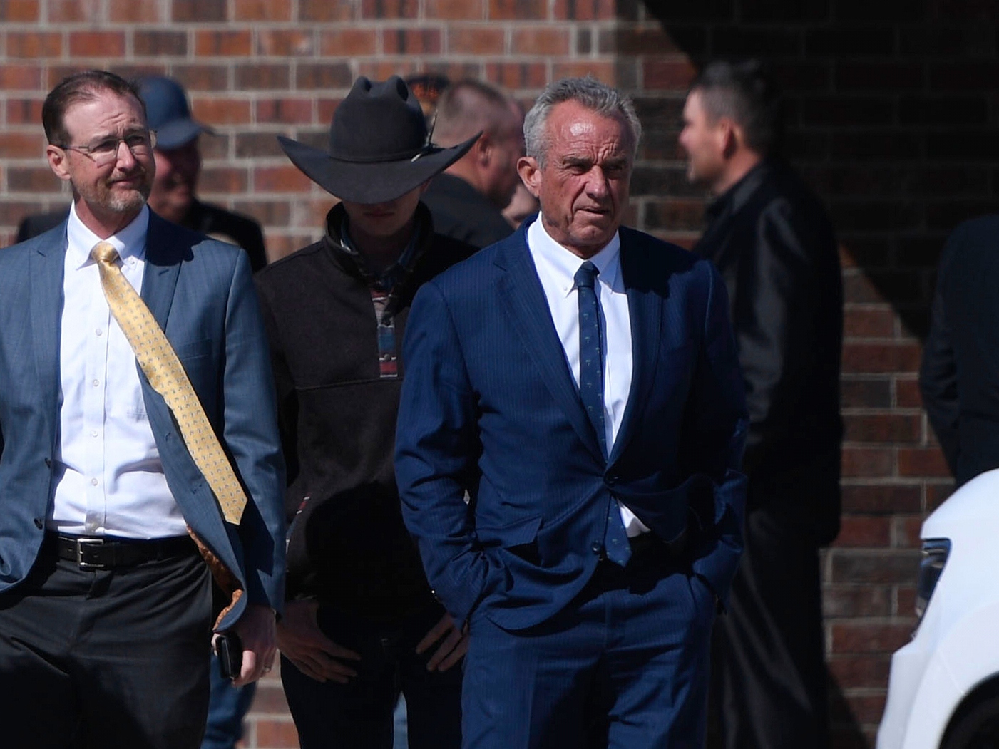 caption: Health and Human Services Secretary Robert F. Kennedy Jr., right, arrives at Reinlander Mennonite Church after a second measles death of a child, on Sunday in Seminole, Texas.