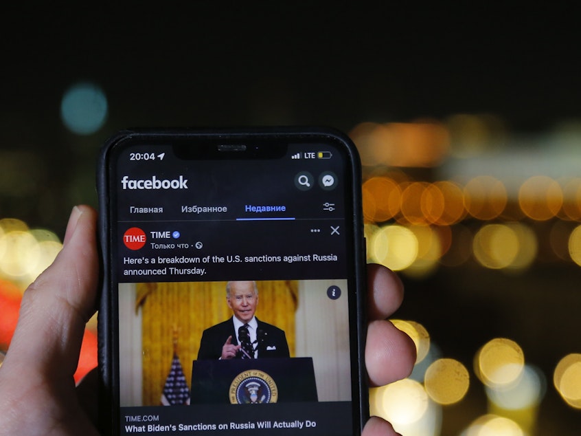 caption: Russia blocked Facebook on Friday citing "discrimination" against state-sponsored media. Here a smartphone user in Moscow watches a Facebook clip of U.S. President Joe Biden on Friday, Feb. 25, 2022.