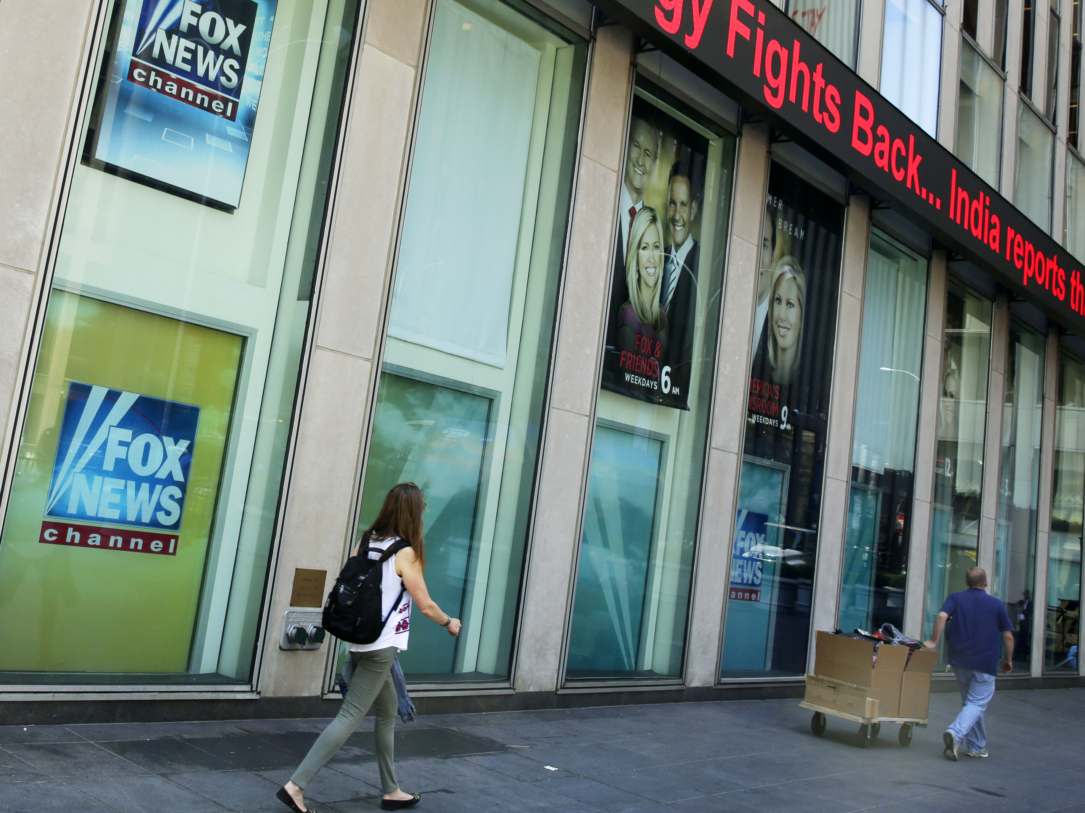 caption: People pass the News Corporation headquarters building and Fox News studios in New York.