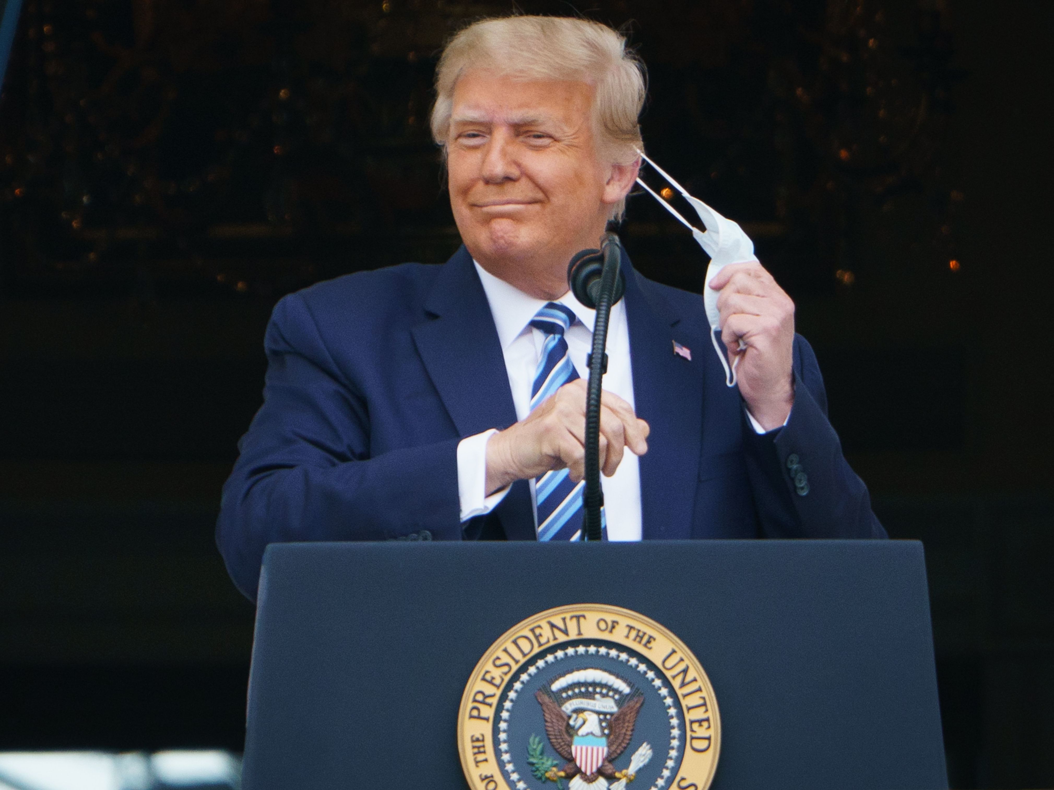 caption: President Trump takes his mask off before speaking from the South Portico of the White House during a rally on Saturday. He is traveling for another rally for the first time on Monday.