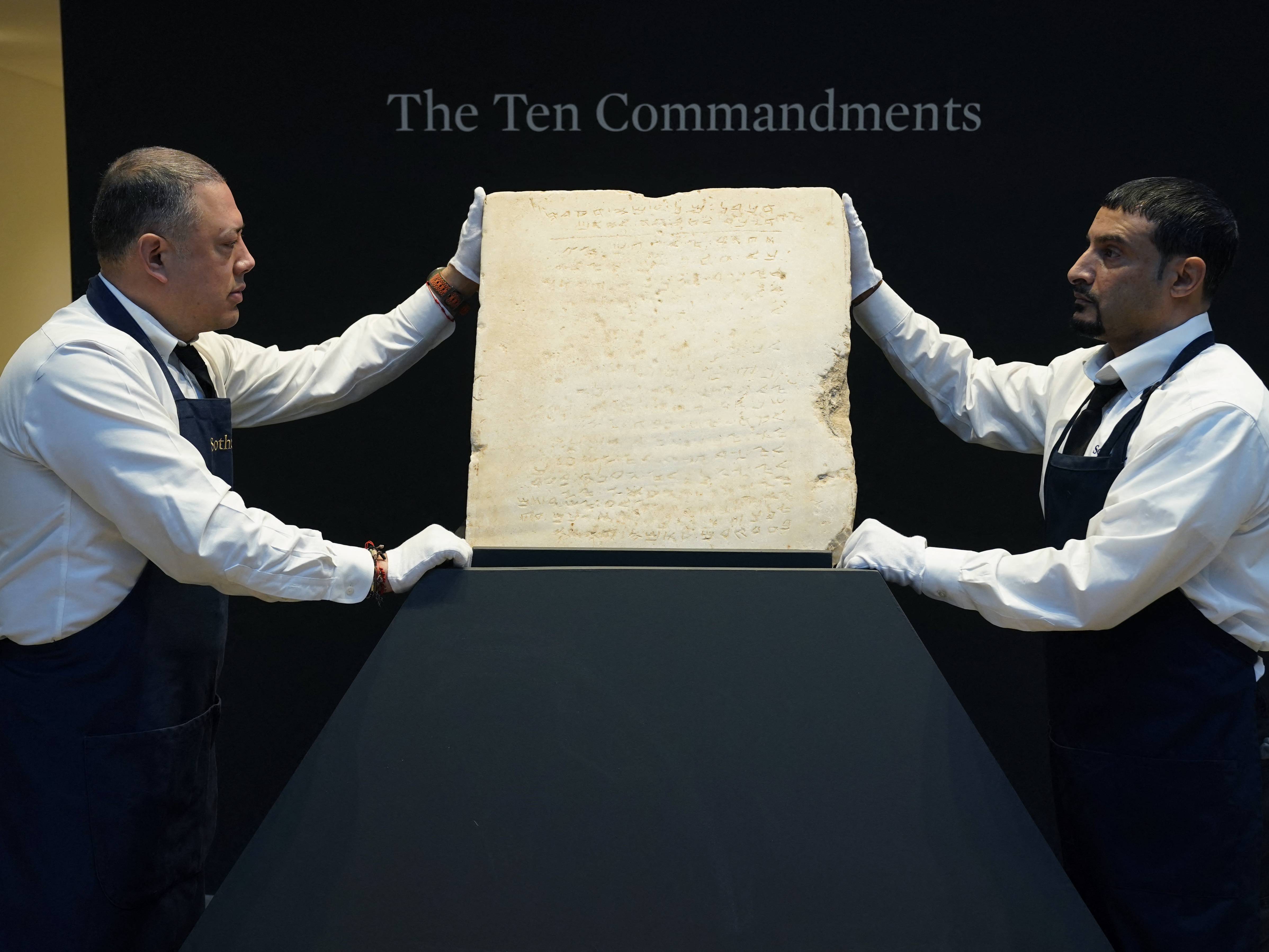 caption: Sotheby's workers hold the stone tablet of the Ten Commandments that is scheduled for auction.