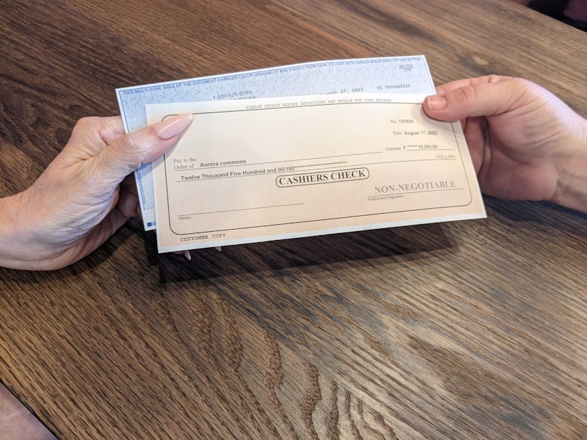caption: Candace Sparks hands one of two checks to Elizabeth Dahl to help people seeking help from the Aurora Commons.