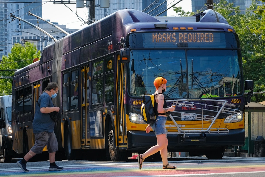 caption: Pedestrians cross in front of a King County Metro bus in Capitol Hill, August 2, 2021. 