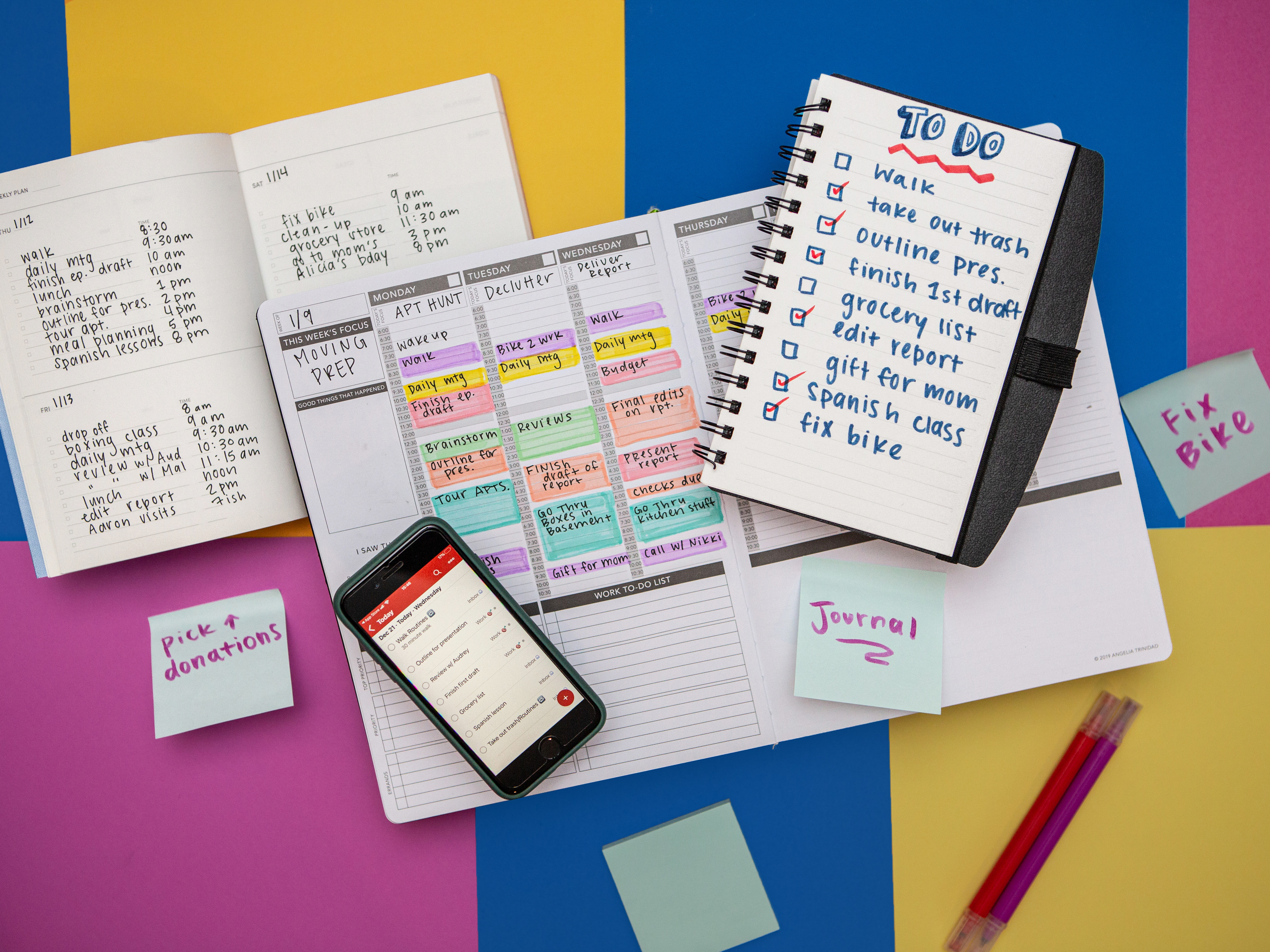 A flat lay photograph of different types of to do lists is photographed from above. Including a planner with time boxing, a to do list in a spiral notebook, a to do list app on a phone and post it notes. The types of to do lists are laid on a background of colorful squares in yellow, fuchsia and yellow.