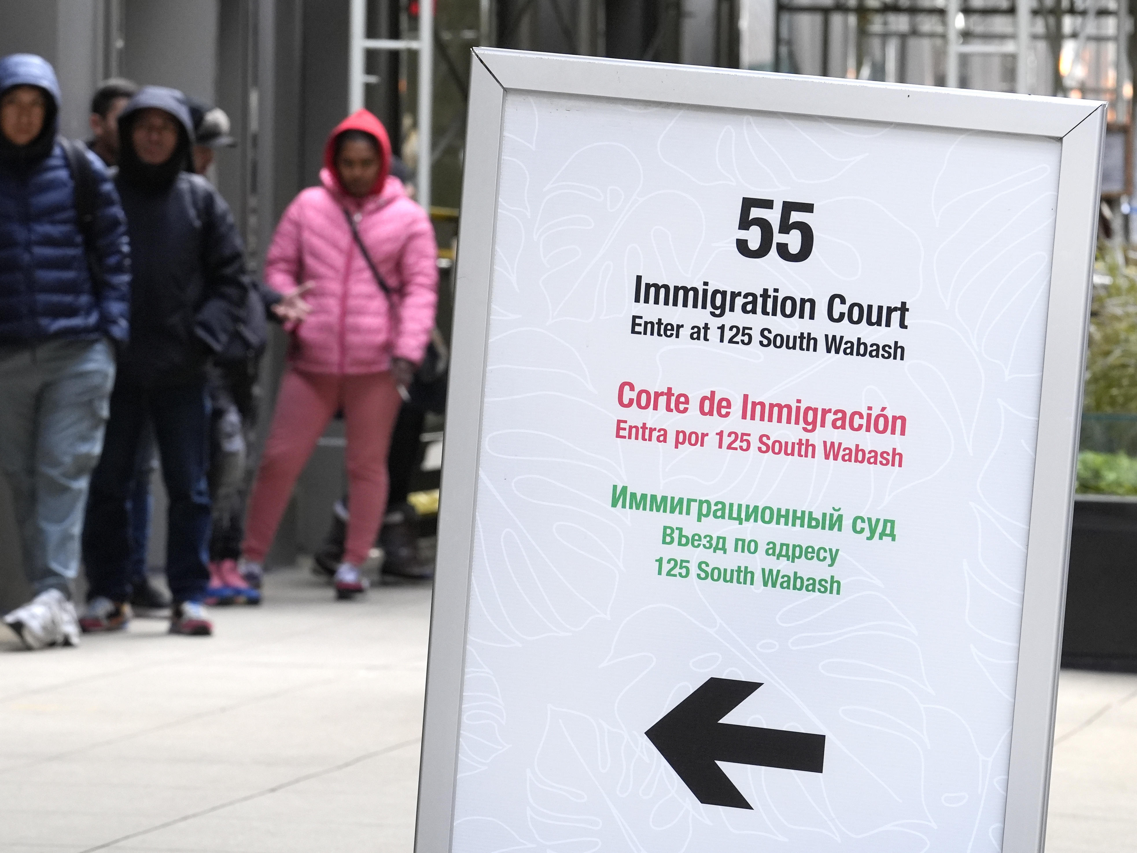 caption: People wait in a cue before being led into a downtown Chicago building where an immigration court presides in November 2024 in Chicago.