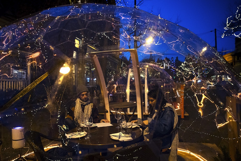 caption: Ben Dines, left, and Alex Manno, right, dine inside of a clear dome structure outside of San Fermo on Sunday, November 15, 2020, along Ballard Avenue Northwest in Seattle.