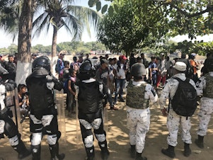 caption: Mexico's National Guard prevents migrants who walked across the river from making their way further into Mexico.