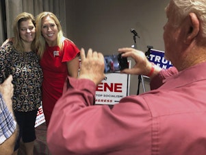 caption: Supporters take photos with construction executive Marjorie Taylor Greene, background right, late Tuesday, in Rome, Ga. Greene, criticized for promoting racist videos and adamantly supporting the far-right QAnon conspiracy theory, won the GOP nomination for northwest Georgia's 14th Congressional District.