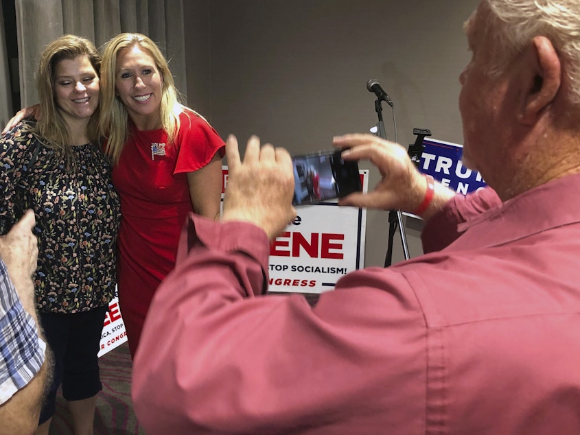 caption: Supporters take photos with construction executive Marjorie Taylor Greene, background right, late Tuesday, in Rome, Ga. Greene, criticized for promoting racist videos and adamantly supporting the far-right QAnon conspiracy theory, won the GOP nomination for northwest Georgia's 14th Congressional District.