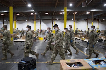 caption: Washington National Guard soldiers walk through the Food Lifeline Covid Response Center on Tuesday, April 21, 2020,  along East Marginal Way South in Seattle. “What makes this particular response different is just the very steep increase in need in our communities,” said Amythst Shipman, director of operations strategy at Food Lifeline. 