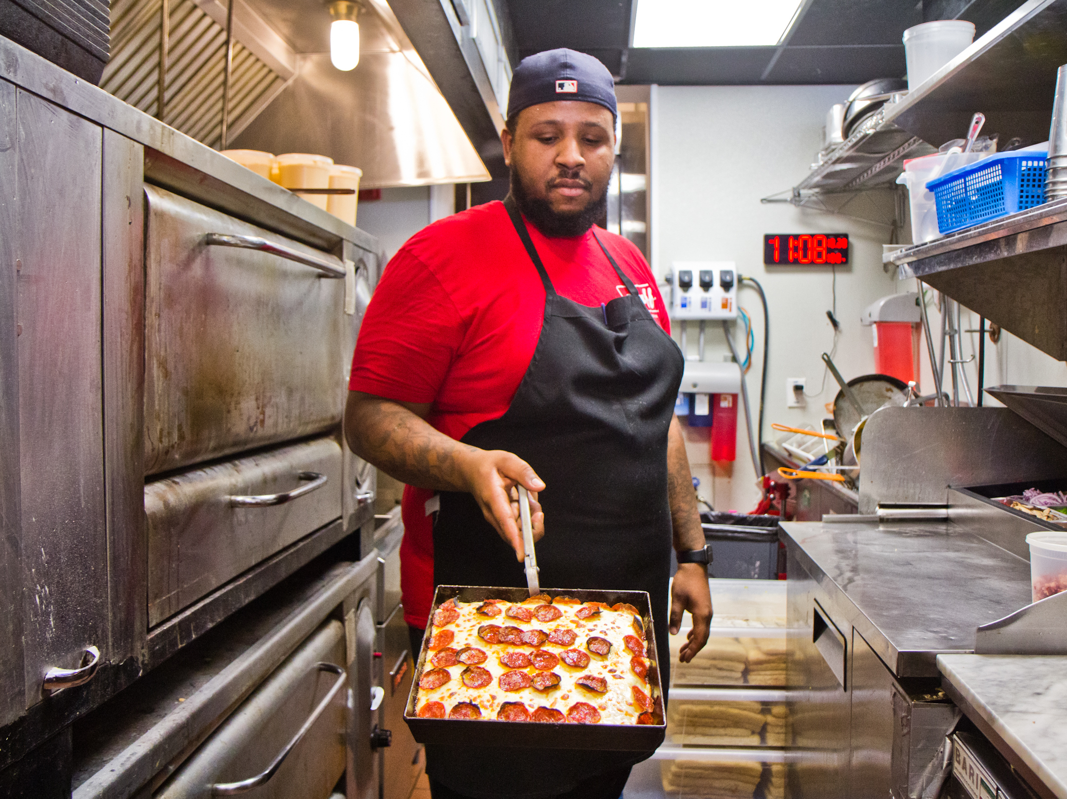 caption: Down North Pizza employee Miles Jackson presents a pie from the oven.