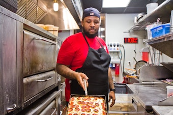 caption: Down North Pizza employee Miles Jackson presents a pie from the oven.