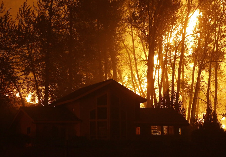 caption: A wildfire burns behind a home on Twisp River Road early Thursday, Aug. 20, 2015 in Twisp, Wash. 