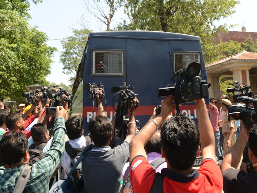 caption: Journalists gather around an Indian police vehicle carrying seven people accused in the 2018 rape and murder of an 8-year-old girl in the state of Jammu and Kashmir. Six men were convicted and one was acquitted on Monday. Another suspect will be tried in juvenile court.