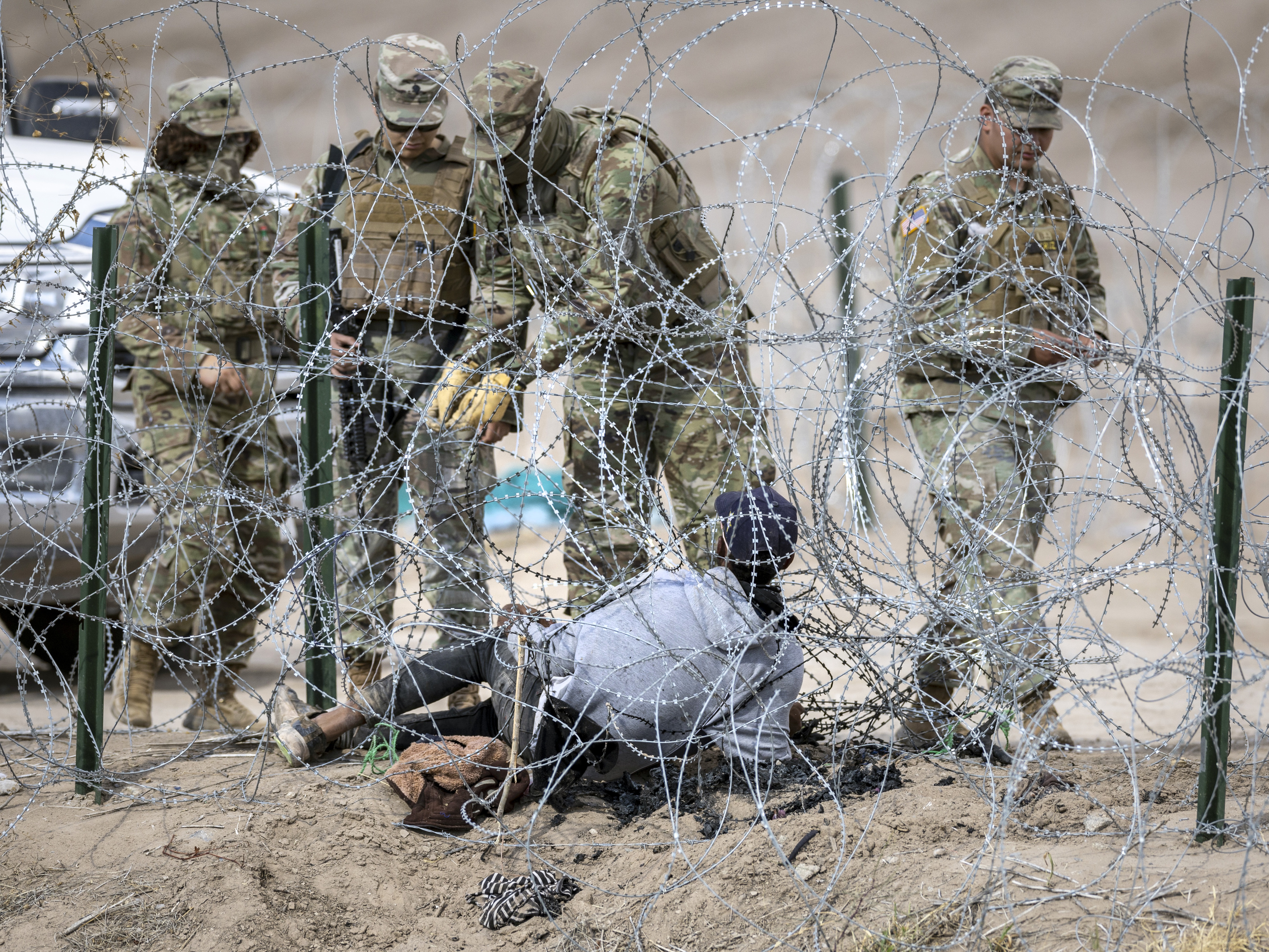 caption: Texas National Guard troops try to untangle an immigrant caught in razor wire after he crossed the U.S.-Mexico border into El Paso, Texas, on Jan. 31, 2024. The Trump administration now plans to use Guard troops for law enforcement activities, including "night operations and rural interdiction," as well as "guard duty and riot control" inside immigrant detention facilities.