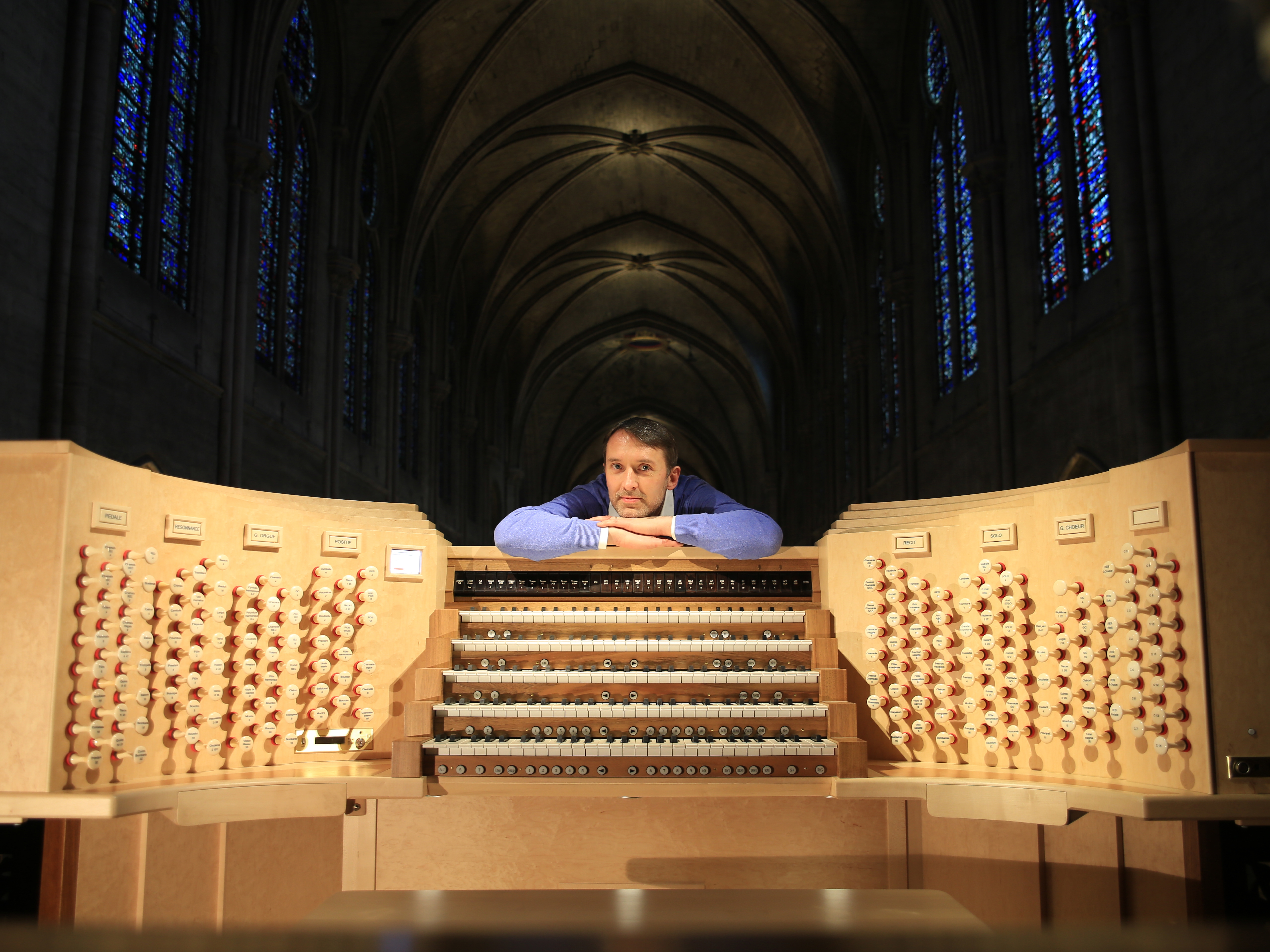 caption: Olivier Latry, Notre Dame's longest-serving organist, poses beside the refurbished instrument, ready for the reopening ceremonies after the destructive fire in 2019.