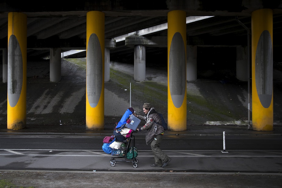 caption: Adrian Anthony moves some of his belongings to another area four blocks away after the encampment where he was living under the I-5 overpass was swept on Wednesday, March 13, 2019, in the Ravenna neighborhood of Seattle. Anthony estimated that a sweep caused him to move from one area to another around 20 times. 