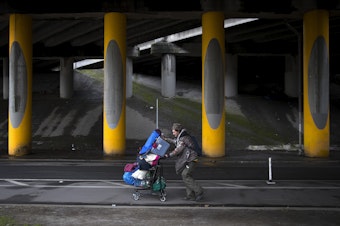caption: Adrian Anthony moves some of his belongings to another area four blocks away after the encampment where he was living under the I-5 overpass was swept on Wednesday, March 13, 2019, in the Ravenna neighborhood of Seattle. Anthony estimated that a sweep caused him to move from one area to another around 20 times. 