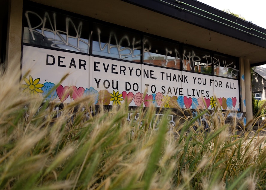 caption: The mural painted on the windows of the Ballard Blossom flower shop offers gratitude to the occasional passing pedestrian. While the store is offering no-contact deliveries, they are unable to deliver to hospitals, including the Swedish Medical Center's Ballad campus across the street. Talk of banning flowers from hospitals has circulated for years, but the pandemic has elevated concern that the plants and vases could carry dangerous molds.