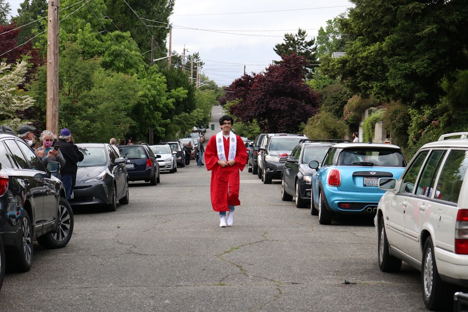 caption: This street in Phinney Ridge, a Seattle neighborhood, has turned into a celebration for graduates after school graduations were canceled because of the coronavirus pandemic. Ballard graduate Lukas Ramakrishnan walks down the street, transformed for the moment into a walkway for graduates, with supporters lining the sidewalks.