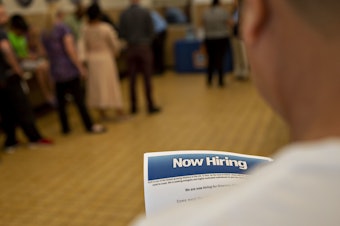 caption: The U.S. has added jobs in every month for nearly eight years. Here, a job seeker holds an employment flier during a hiring event at an Aldi Supermarket in Darien, Ill., in July.