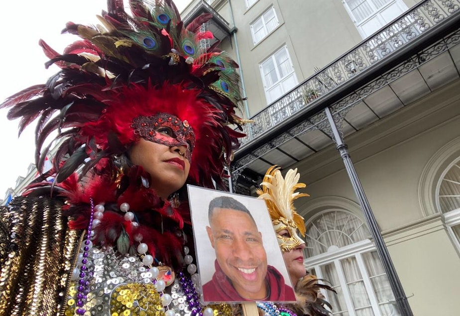 caption: Deanna Teasley and her friend and co-worker Caroline at Mardis Gras in New Orleans. They're holding a photo of their friend Demetrius, who died shorty before the trip (the cause was not COVID).