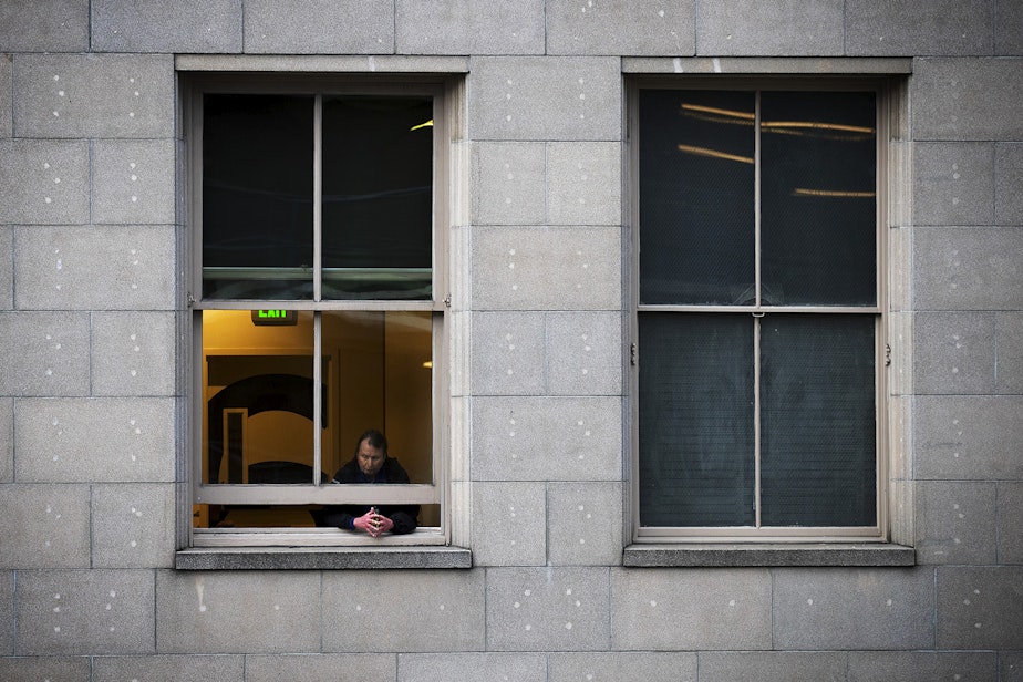 caption: A security guard looks out of a window onto traffic along Third Avenue on Tuesday, March 24, 2020, in Seattle. 