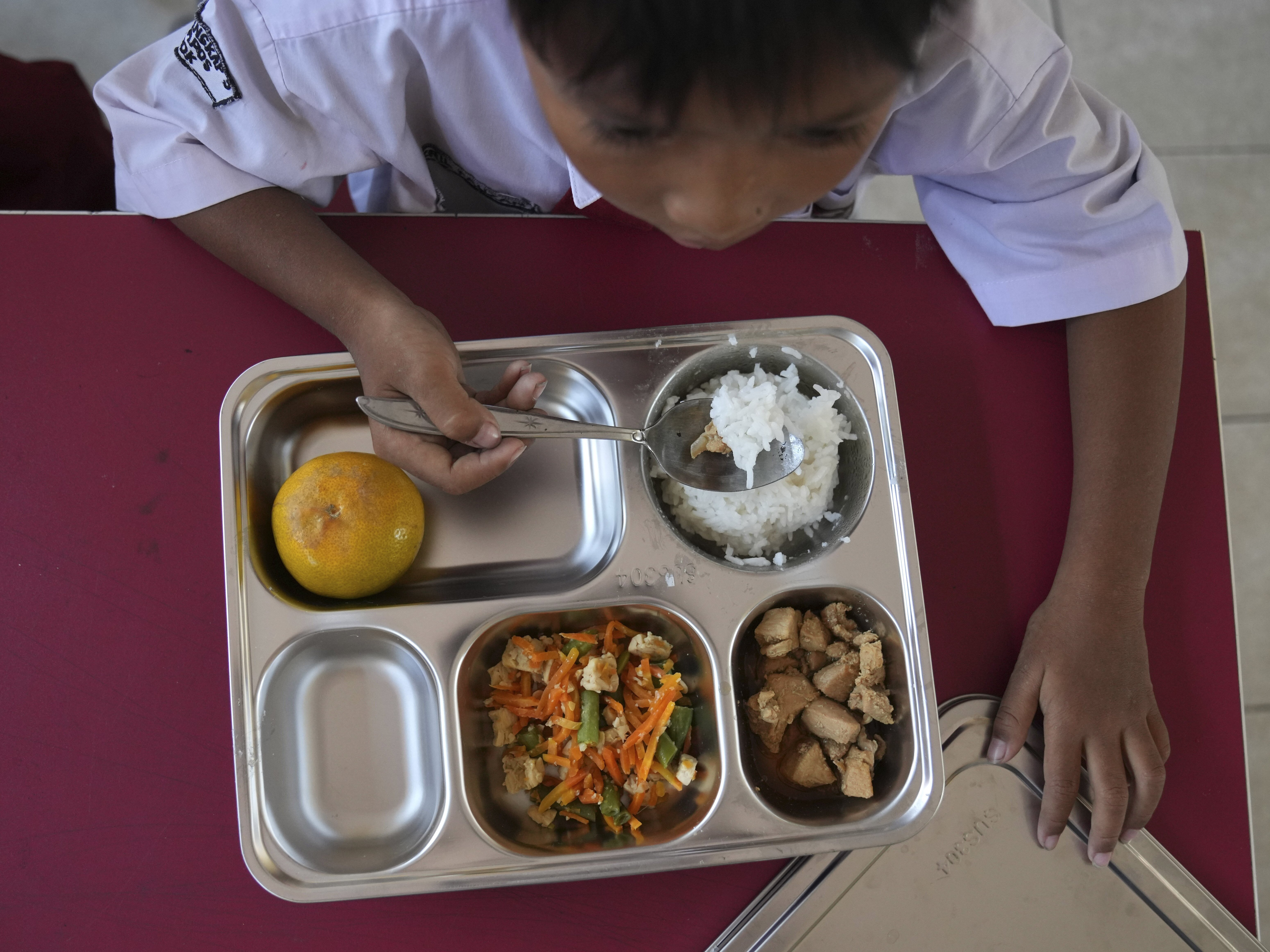 caption: A student has his meal during the kick off of President Prabowo Subianto's ambitious free meal program to feed children and pregnant women nationwide — despite critics saying that its required logistics could hurt Indonesia's state finances and economy — at an elementary school in Depok, West Java, Indonesia, Monday, Jan. 6, 2025.