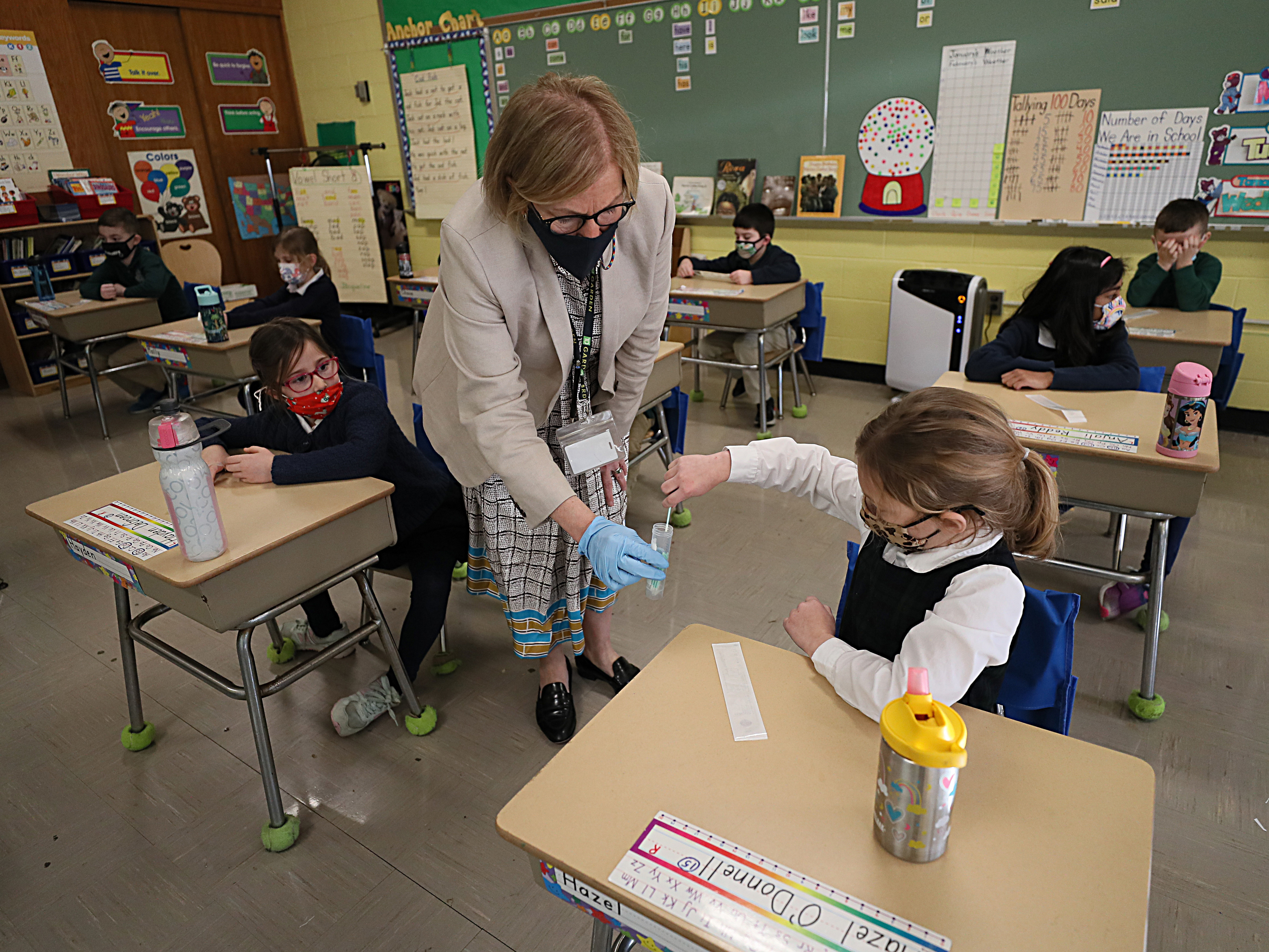 caption: A student gives her coronavirus swab to Helenann Civian, the principal of South Boston Catholic Academy in Boston in January. The White House announced $10 billion to expand testing in K-12 schools.