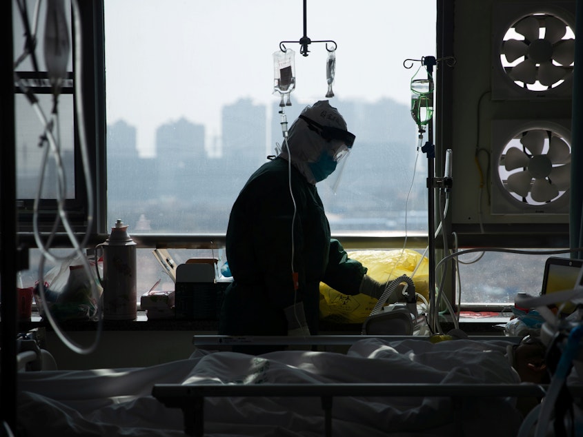 caption: A medical worker in a protective suit attends to a patient in a hospital in Wuhan, China.