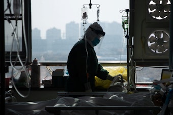caption: A medical worker in a protective suit attends to a patient in a hospital in Wuhan, China.