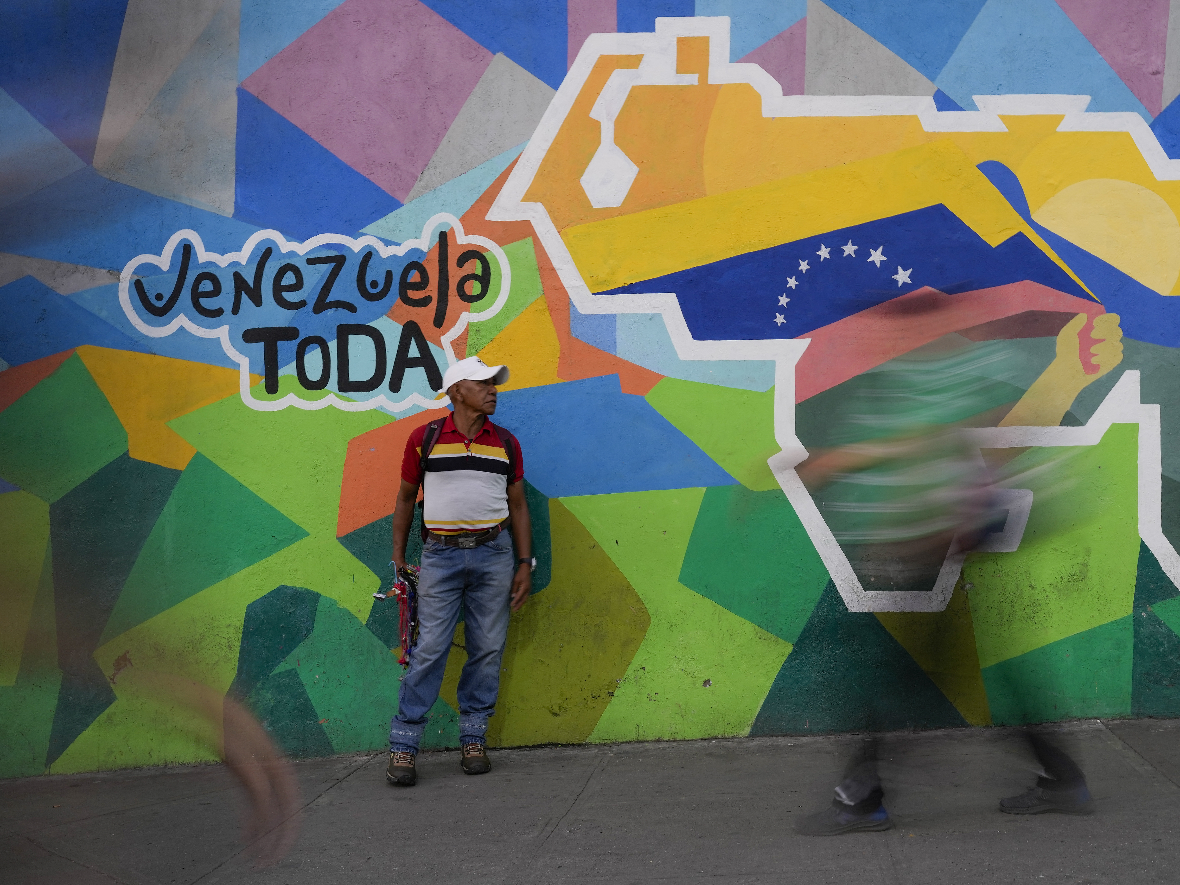 caption: A man sells phone cables in front of a mural of the Venezuelan map with the Essequibo territory included in the Petare neighborhood of Caracas, Venezuela, on Dec. 11.