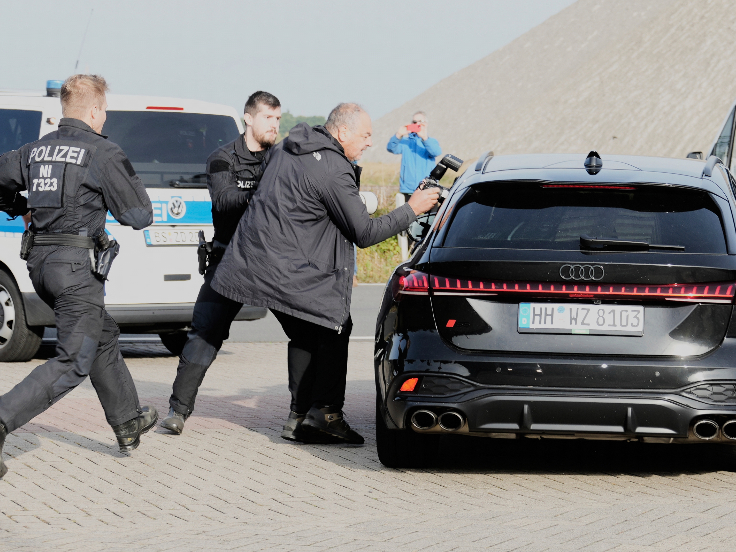 caption: Police officers try to stop a British photographer as he takes pictures inside a car leaving a prison, carrying a suspect in the 2007 disappearance of British toddler Madeleine McCann, in Sehnde, Germany, Wednesday, Sept. 17, 2025.