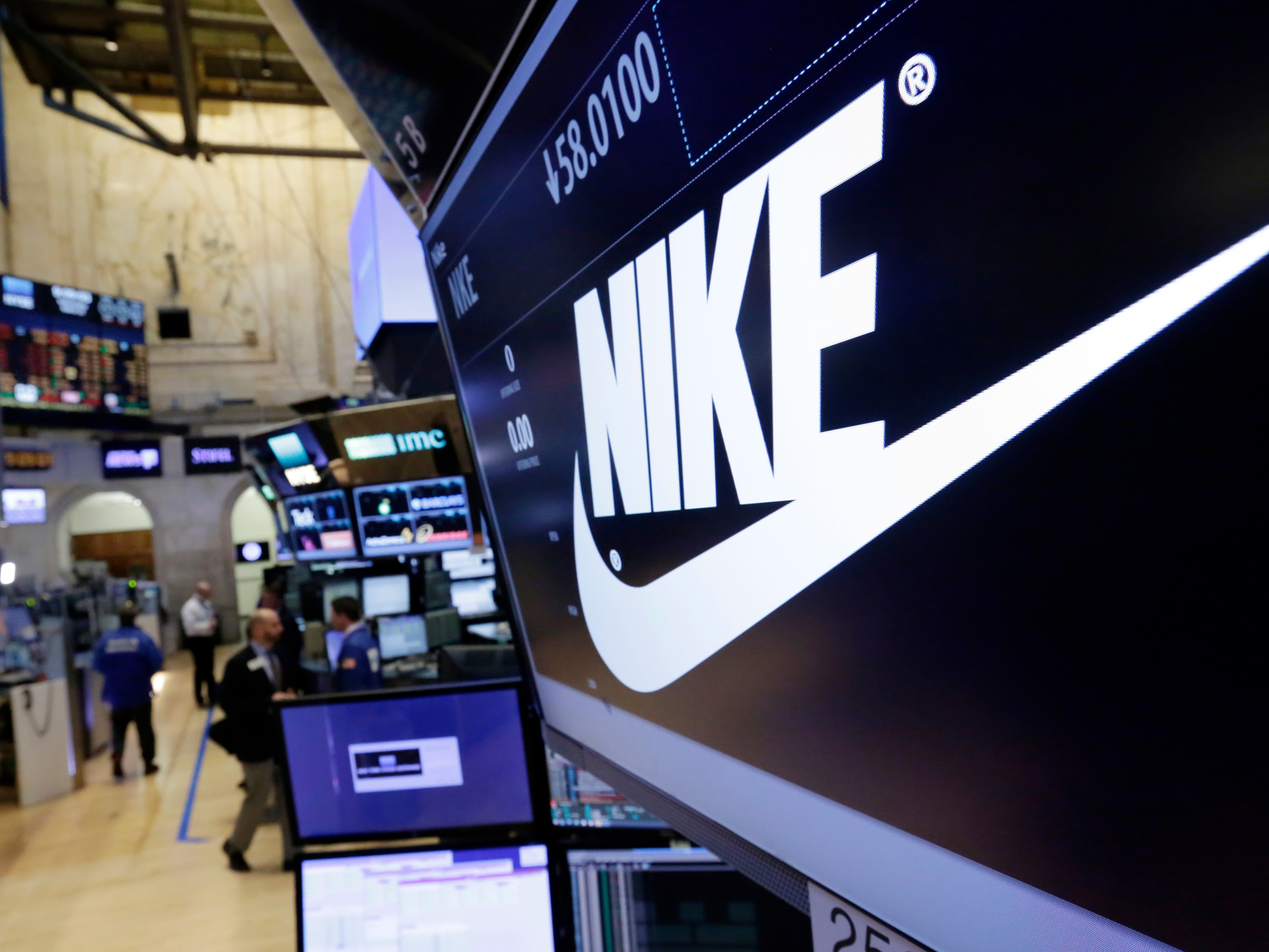 caption: The Nike logo appears above the post where it trades on the floor of the New York Stock Exchange, March 22, 2017.