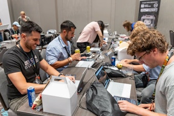 caption: Participants at the 2023 Def Con hacker convention, trying to subvert AI chatbots as part of a contest to test the systems' vulnerabilities.