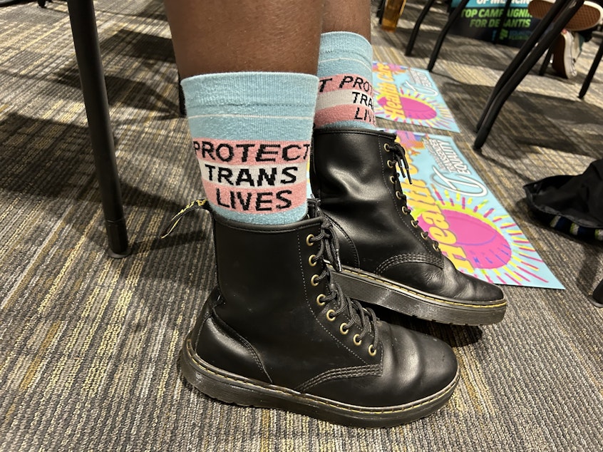 caption: A trans-rights supporter wears socks reading "protect trans lives" at a meeting of Florida's medical boards on Feb. 10, 2023 in Tallahassee, Fla.